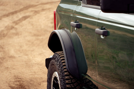 DV8 Offroad tube fender flares installed on green 4-door Ford Bronco, close-up front door and fender on dirt trail