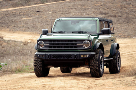 DV8 Offroad tube fender flares installed on green 4-door Ford Bronco, front three-quarter view under cloudy sky