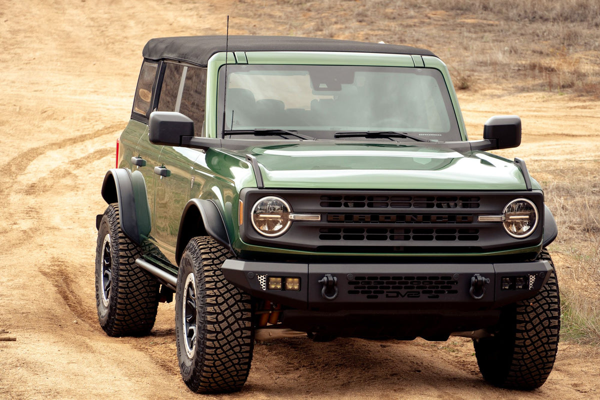 DV8 Offroad tube fender flares installed on green 4-door Ford Bronco, front three-quarter view on dirt trail