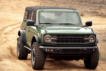 DV8 Offroad tube fender flares installed on green 4-door Ford Bronco, front three-quarter view on dirt trail