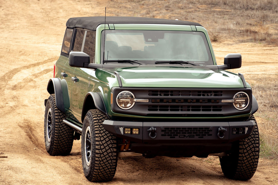 DV8 Offroad tube fender flares installed on green 4-door Ford Bronco, front three-quarter view on dirt trail