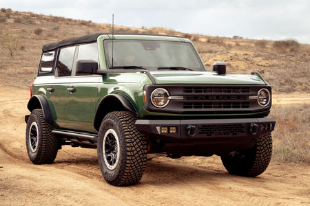 DV8 Offroad tube fender flares installed on green 4-door Ford Bronco, front three-quarter view on hillside trail