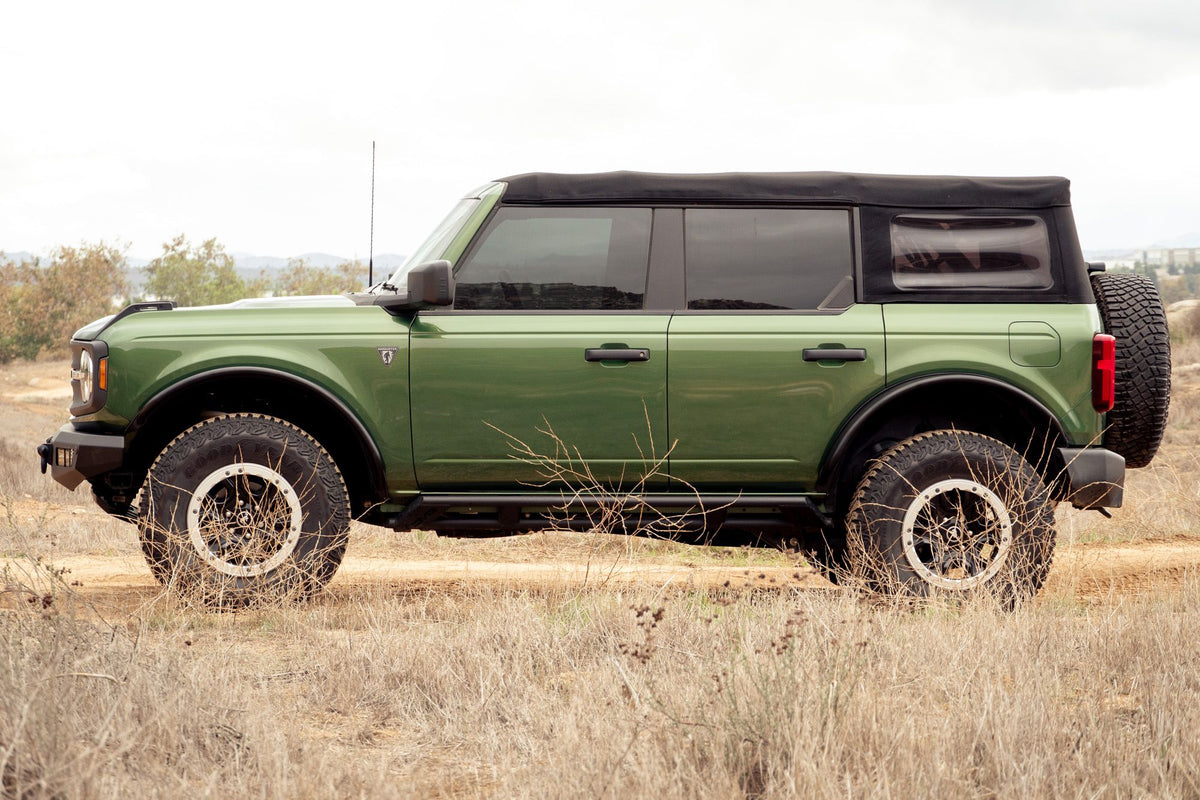 DV8 Offroad tube fender flares installed on green 4-door Ford Bronco, full side profile view under cloudy sky