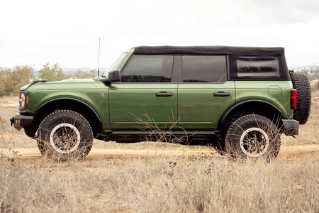 DV8 Offroad tube fender flares installed on green 4-door Ford Bronco, full side profile view under cloudy sky