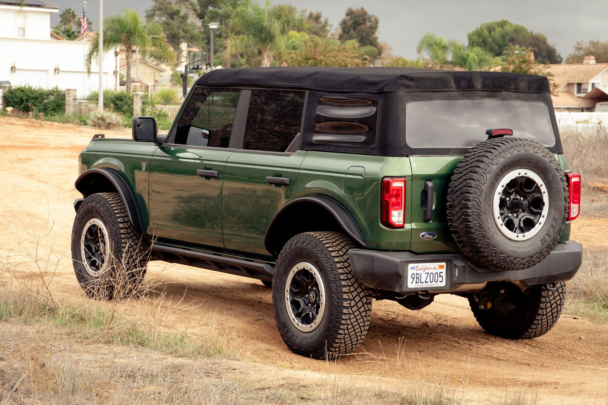 DV8 Offroad tube fender flares installed on green 4-door Ford Bronco, full side profile view with trees in background