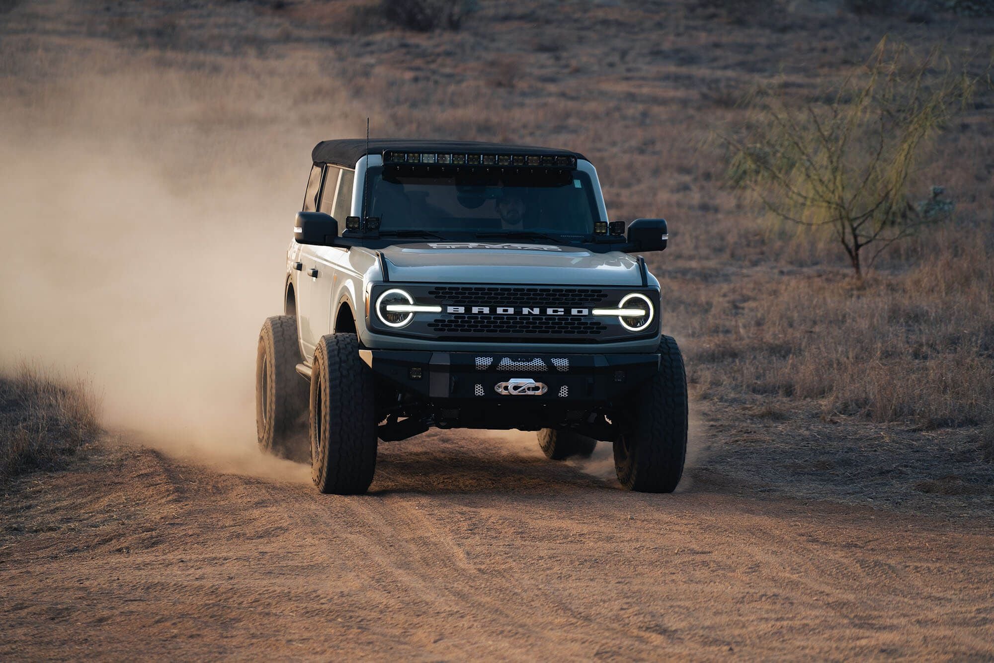 DV8 Offroad fender flare delete installed on Ford Bronco, front view driving on dirt trail with dust cloud
