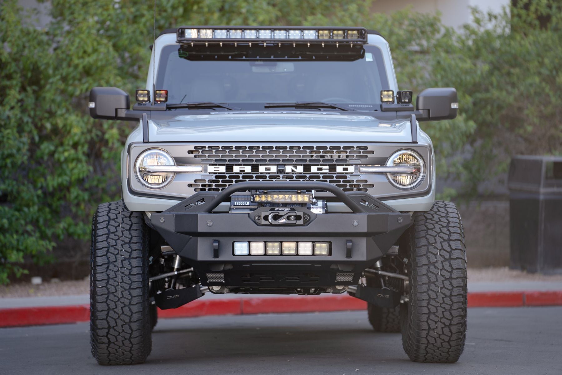 DV8 Offroad fender flare delete installed on Ford Bronco with light bar and winch bumper, front view at dusk