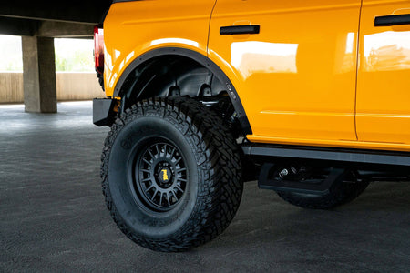 DV8 Offroad fender flare delete installed on orange Ford Bronco, angled rear wheel and fender close-up in parking garage
