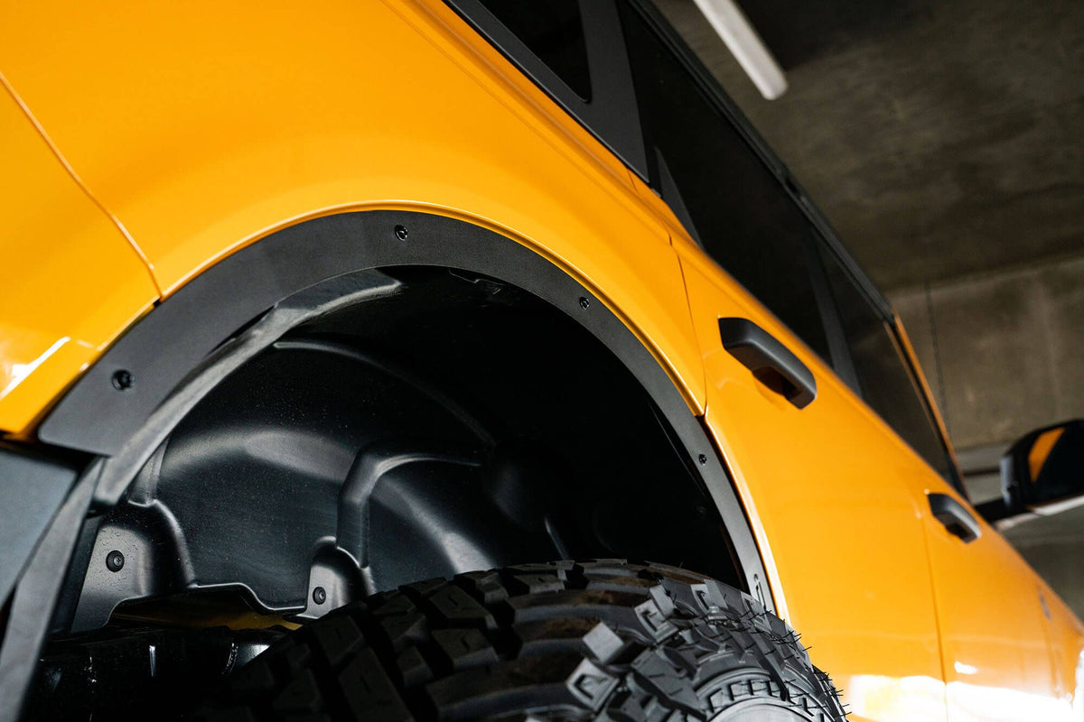 DV8 Offroad fender flare delete installed on orange Ford Bronco, close-up front fender well and tire