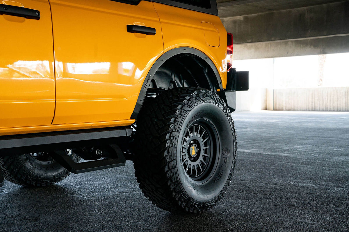 DV8 Offroad fender flare delete installed on orange Ford Bronco, rear quarter panel close-up in parking garage