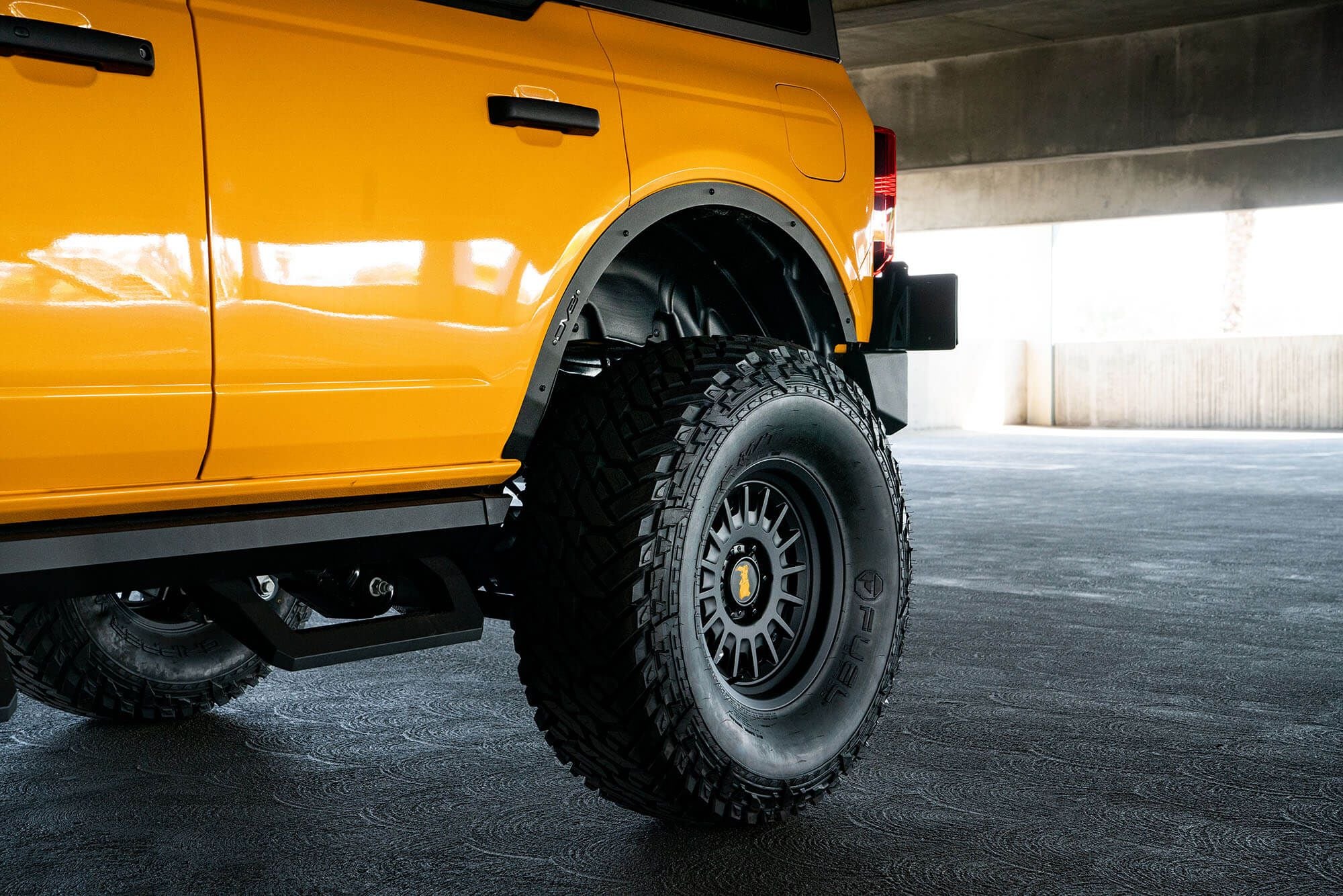 DV8 Offroad fender flare delete installed on orange Ford Bronco, rear quarter panel close-up in parking garage