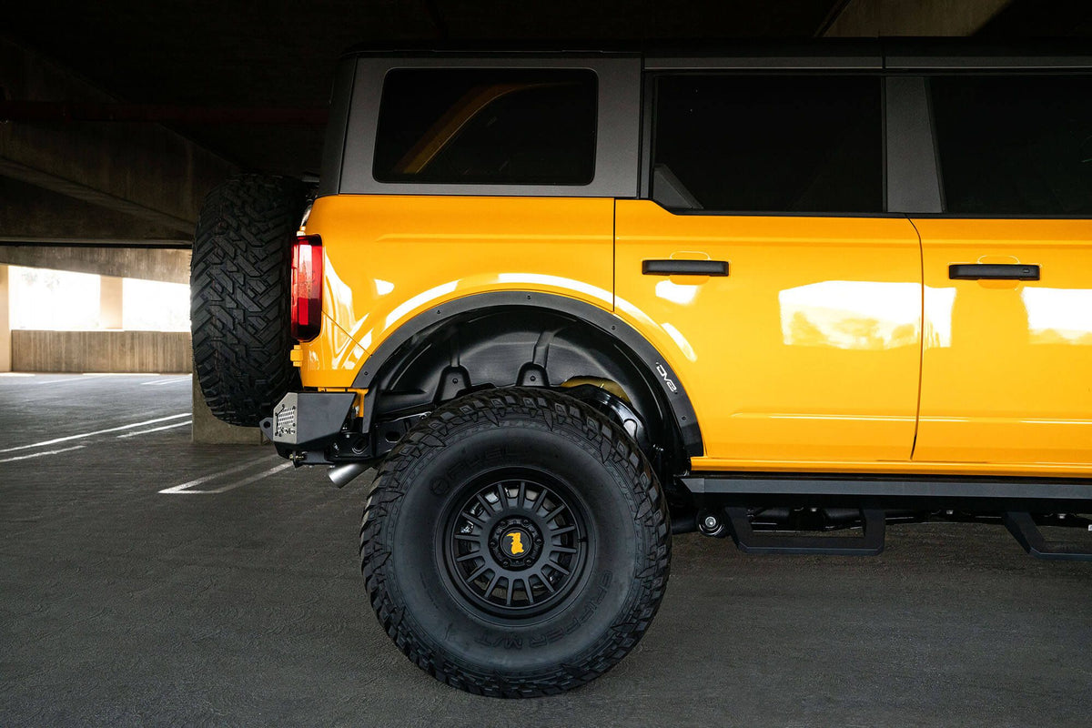DV8 Offroad fender flare delete installed on orange Ford Bronco, rear three-quarter side profile in parking garage