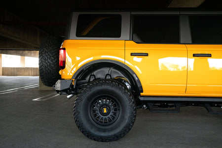 DV8 Offroad fender flare delete installed on orange Ford Bronco, rear three-quarter side profile in parking garage