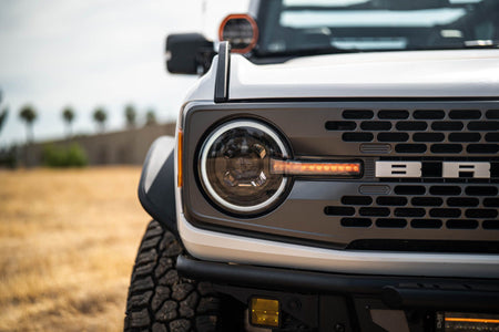 DV8 Offroad Black Series LED headlight installed on white Ford Bronco, front three-quarter close-up illuminated in field