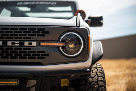 DV8 Offroad Black Series LED headlight installed on white Ford Bronco, close-up showing grille and headlight in field