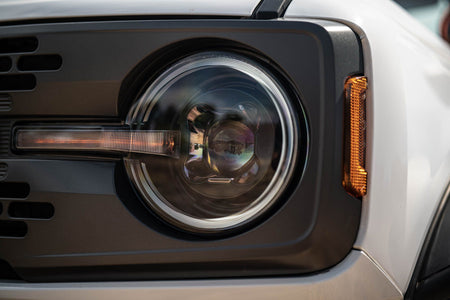 DV8 Offroad Black Series LED headlight installed on white Ford Bronco, close-up showing projector lens and DRL bar