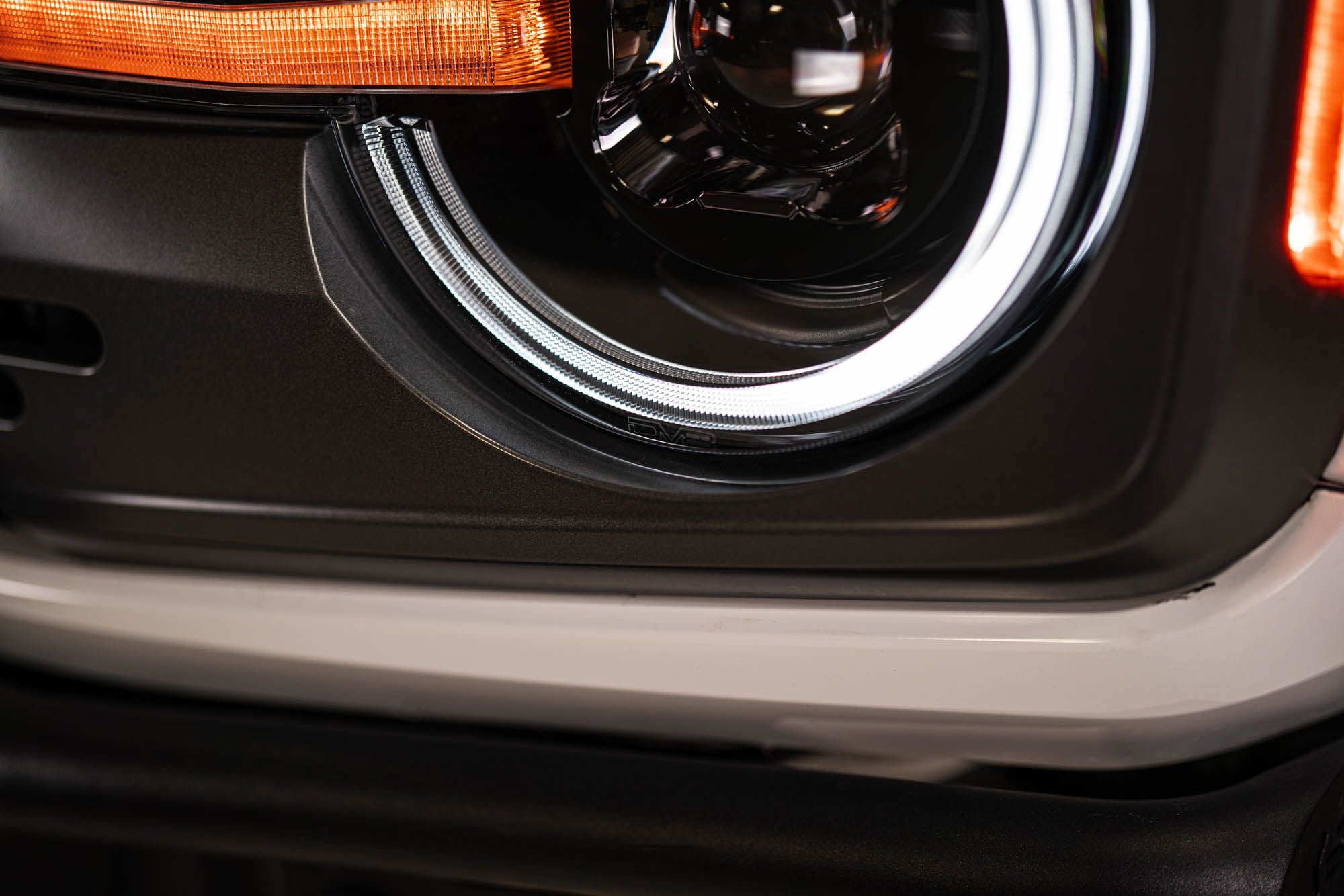 DV8 Offroad Black Series LED headlight installed on white Ford Bronco, close-up showing DRL ring detail and rear taillight