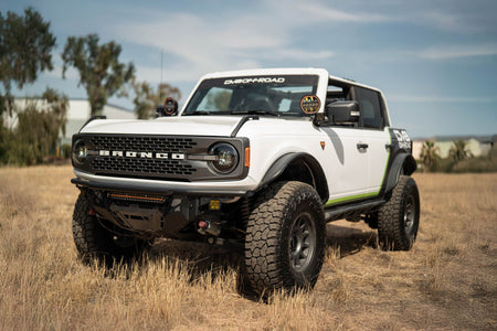 DV8 Offroad Black Series LED headlights installed on white Ford Bronco, distant front three-quarter view of full vehicle in field