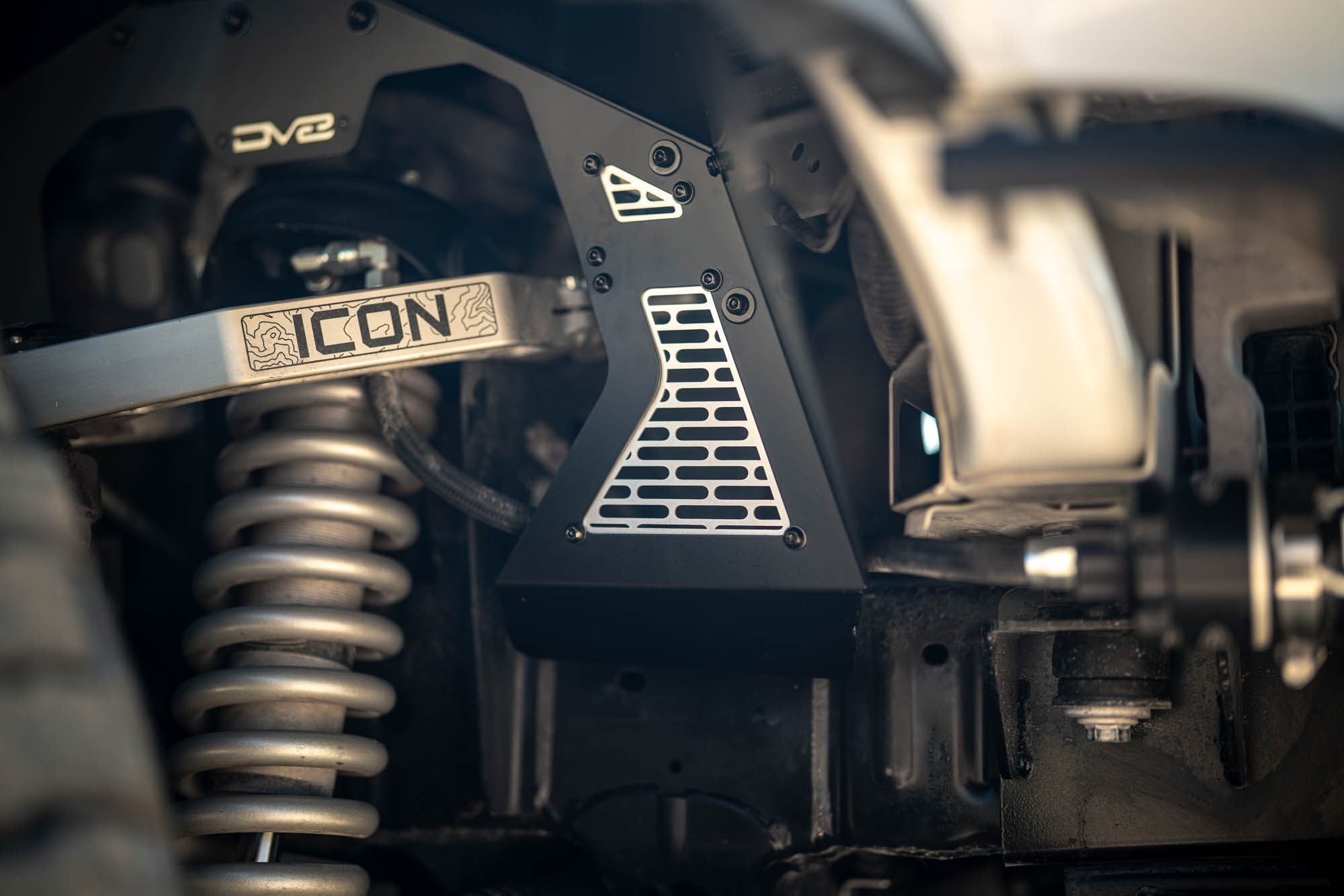 DV8 Offroad front inner fenders installed on Ford Bronco, close-up showing coilover suspension and Icon badge on mesh panel