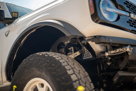 DV8 Offroad front inner fenders installed on white Ford Bronco, close-up wheel well showing tire clearance and Icon branding