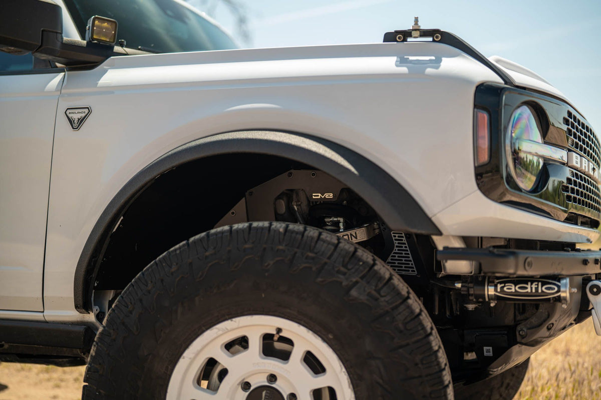 DV8 Offroad front inner fenders installed on white Ford Bronco, front three-quarter close-up showing coilover shock and tire