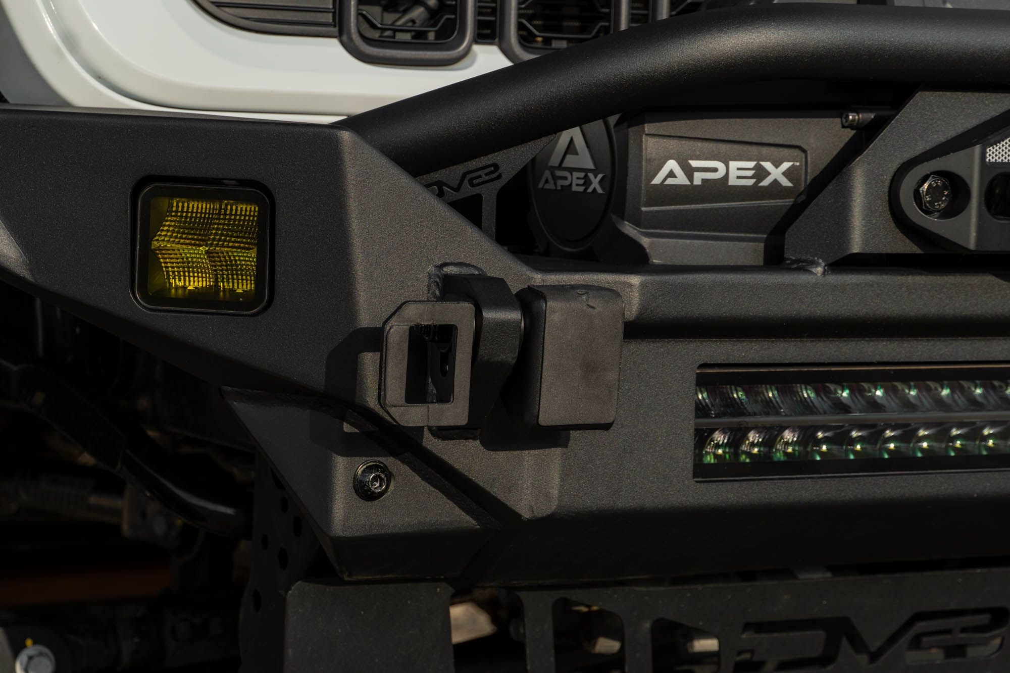 DV8 Offroad universal D-ring license plate mount installed close-up showing bracket mounting detail on aftermarket bumper