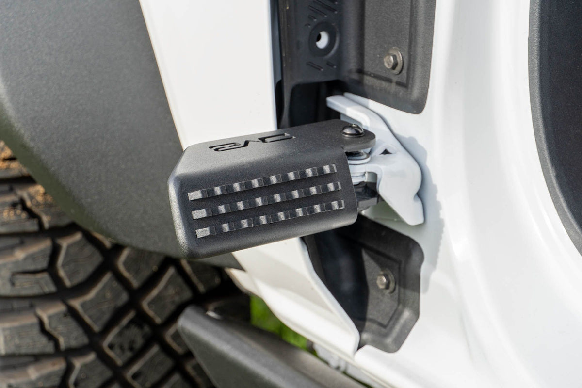 DV8 Offroad foot peg installed on 2021-2026 Ford Bronco door hinge detail view showing peg angle and grip surface