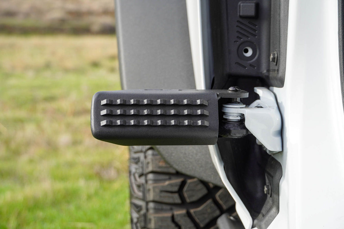DV8 Offroad foot peg installed on 2021-2026 Ford Bronco showing peg position mounted on front door hinge