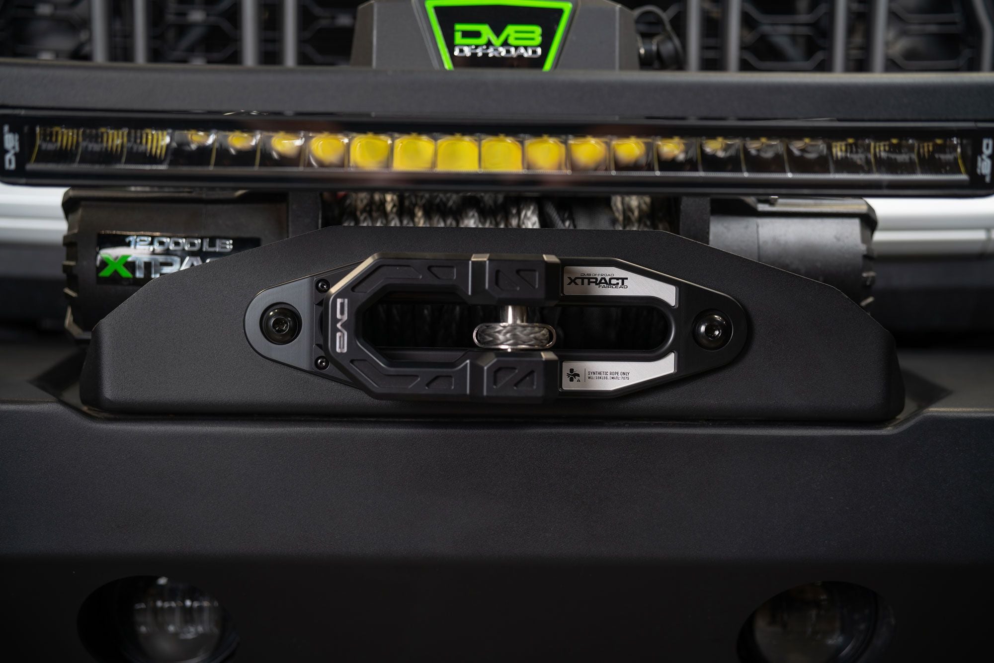 DV8 Offroad Xtract fairlead installed on bumper, close-up with illuminated amber LED light bar and DV8 badge