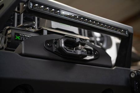 DV8 Offroad Xtract fairlead installed on bumper, angled close-up with LED light bar reflection