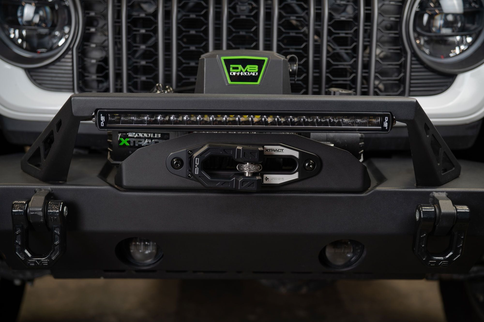 DV8 Offroad Xtract fairlead installed on Jeep front bumper, close-up with LED light bar and DV8 badge