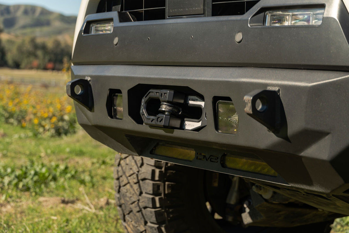 DV8 Offroad Xtract fairlead installed on olive green truck front bumper, wildflower field with mountains in background