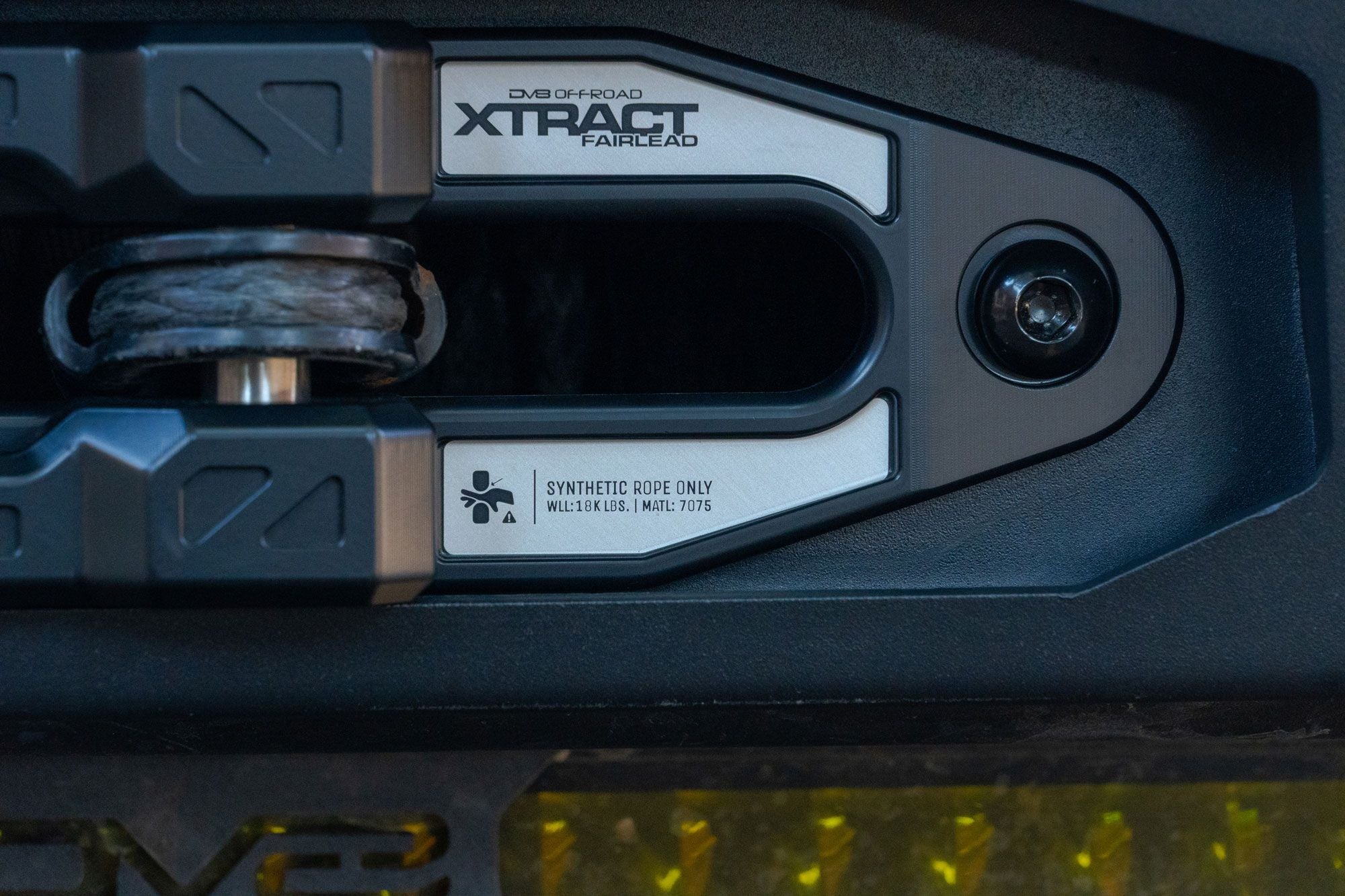 DV8 Offroad Xtract fairlead installed on textured dark bumper, close-up with amber accent lighting