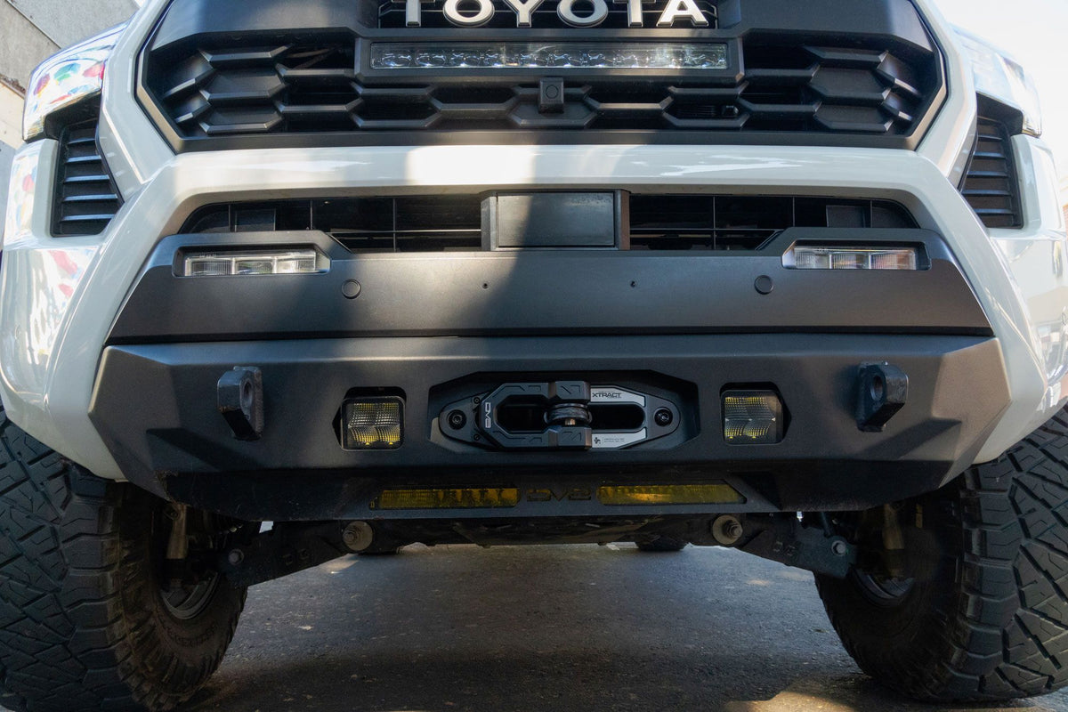 DV8 Offroad Xtract fairlead installed on white Toyota Tacoma front bumper, daytime outdoor front view