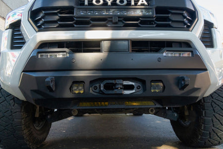 DV8 Offroad Xtract fairlead installed on white Toyota Tacoma front bumper, daytime outdoor front view